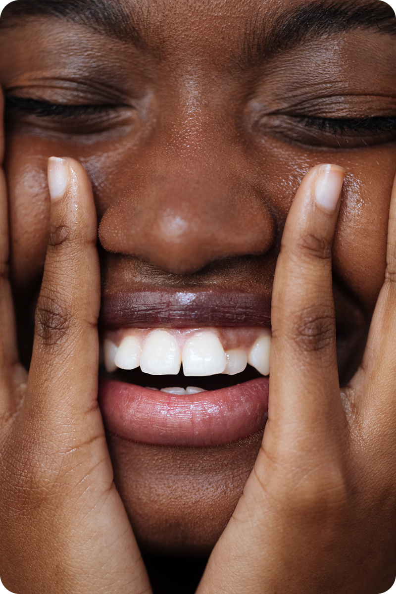 Femme riant aux éclats, les yeux fermés, la joue posée sur son épaule